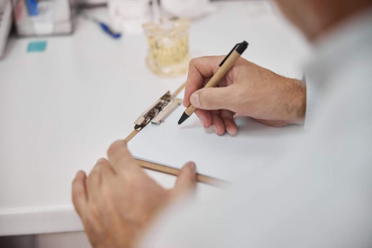 Cropped photo of doctors hand holding a pen and making notes on a blank paper
