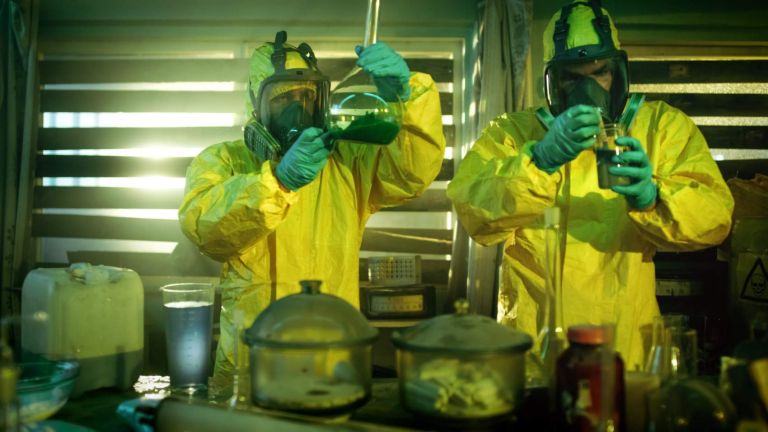 In the Underground Drug Laboratory Two Clandestine Chemists Wearing Protective Masks and Coveralls Test Cooked Drug's Purity and Strength. They Work in the Abandoned Building Full of Glassware and Cooking Equipment.