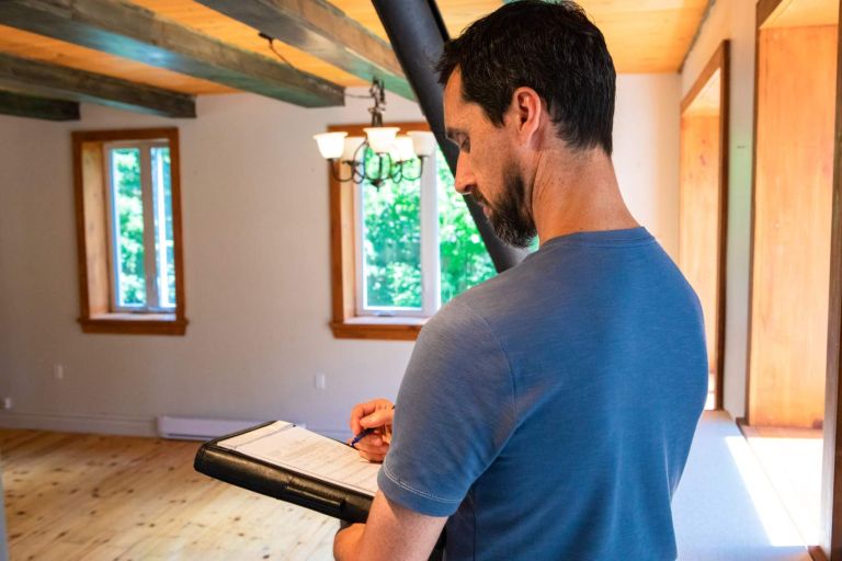 A close up and side profile view of a professional man carrying out an indoor environmental quality inspection (IEQ), checking items off a list with a pen.